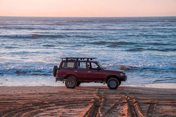 Red offroad car parked at shoreline on sand at beach in evening — Φωτογραφία Αρχείου