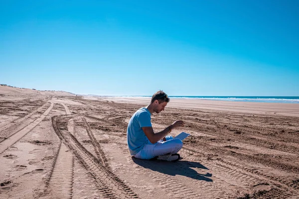 Man using laptop sitting on beach on a bright sunny day — Fotografia de Stock