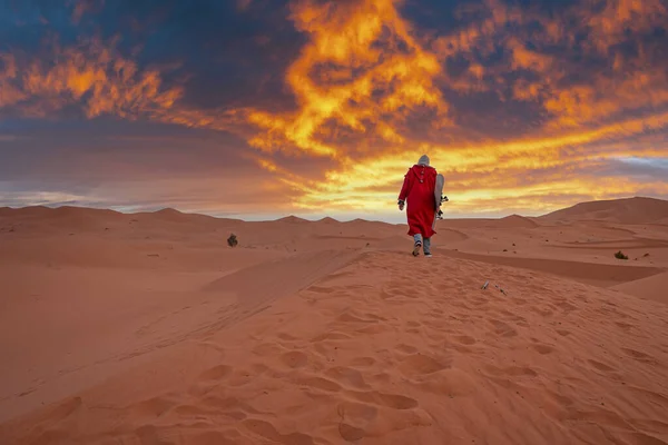 Man in traditional clothes with sandboard walking on sand dunes during dusk — Zdjęcie stockowe