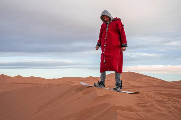 Człowiek w tradycyjnych ubraniach piasek na desce na pustyni przed zachmurzonym niebem — Zdjęcie stockowe