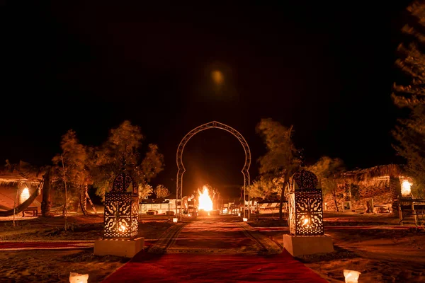 Illuminated lanterns beside carpet on sand in desert against sky during night — Stockfoto