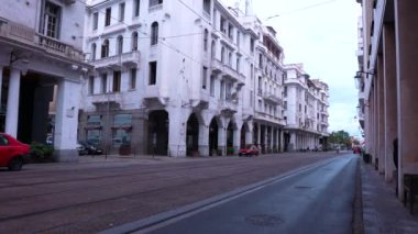 Güneşli bir günde arka planda saat kulesi olan binaların içinden tramvay geçiyor.