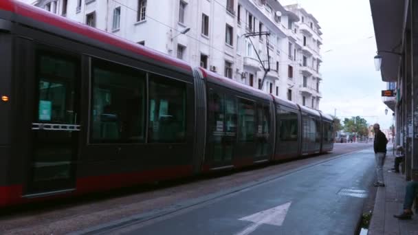 Tramway through buildings with clock tower in background on sunny day — Stock Video