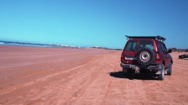 Kırmızı off-road arabası alacakaranlıkta kumlu sahilde gidiyor.
