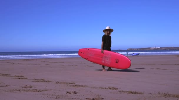 Sonriente profesor de surf masculino llevando tabla de surf mientras camina en la playa — Vídeos de Stock