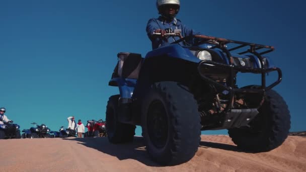 Lidé jezdí na čtyřkolech přes písečné duny za slunečného dne proti moři — Stock video