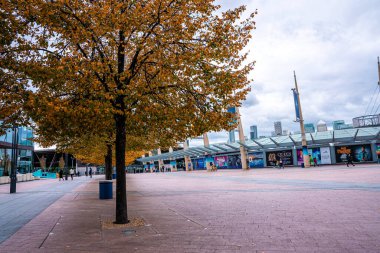 Alışveriş merkezindeki reklam panolarının önünden geçen ve arka planda şehir manzarası olan insanlar.