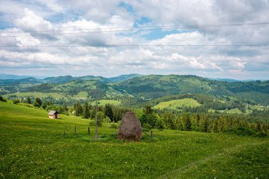 Güzel saman yığını manzarası ve yeşil yamaçtaki eski ev güzel dağ sıraları ve bulutlu gökyüzüne karşı