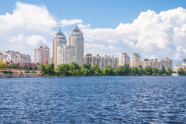 Nehirden görülen yeni modern şehir binaları beyaz bulutlu gökyüzüne karşı, yerleşim bölgesinin modern dış yüzeyi.