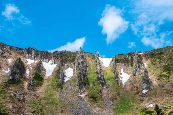 白雪覆盖着岩石悬崖和山峰 陡峭的斜坡和苔藓映衬着多云的天空 低角度的天空 — 图库照片