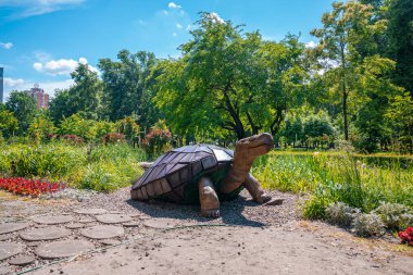 Güneşli bir günde yeşil ağaçlara karşı bahçedeki güzel ahşap kaplumbağa heykeli parktaki kaldırımın yanında kaplumbağa heykeli.