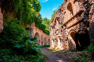 Güneşli bir günde eski kalenin yıkıntıları arasında yürüyen yeşil bitkilerle çevrili antik kalenin kalıntıları.