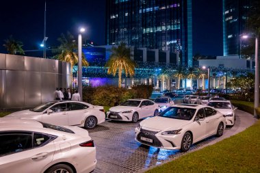 Dubai, BAE. 10 Şubat 2022. Süslü ağaçlar ve şehir binaları olan bulvarda arka arkaya beyaz lüks arabalar.