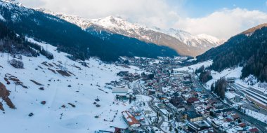 Avusturya 'nın kayak merkezi St. Anton am Arlberg' de kış güneşli gökyüzü ve arka planda çam ağaçlarıyla kaplı karlı dağlar.