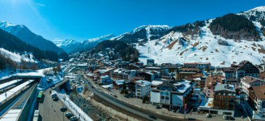 Avusturya 'nın kayak merkezi St. Anton am Arlberg' de kış güneşli gökyüzü ve arka planda çam ağaçlarıyla kaplı karlı dağlar.