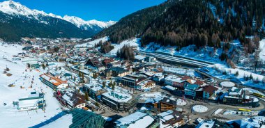 Avusturya 'nın kayak merkezi St. Anton am Arlberg' de kış güneşli gökyüzü ve arka planda çam ağaçlarıyla kaplı karlı dağlar.