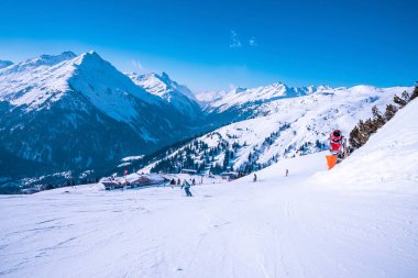 Kayakçılar yokuş aşağı kar üzerinde kayak yapıyorlar. Mavi gökyüzüne karşı güzel beyaz dağ sırası. Turistler Alplerde kış sporunun tadını çıkarıyorlar.