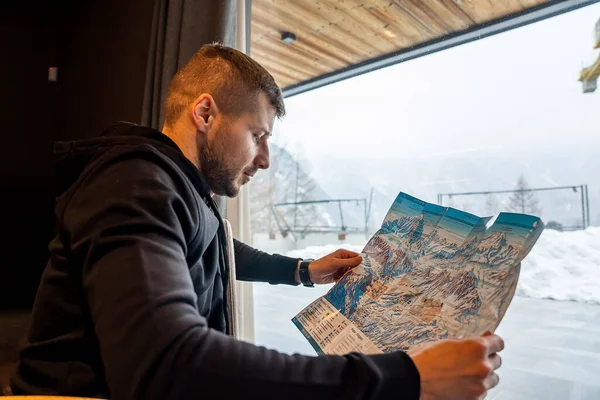 游客正在通过窗户分析纸质地图 这个年轻人在旅行中计划滑雪旅行 他在阿尔堡度假 — 图库照片