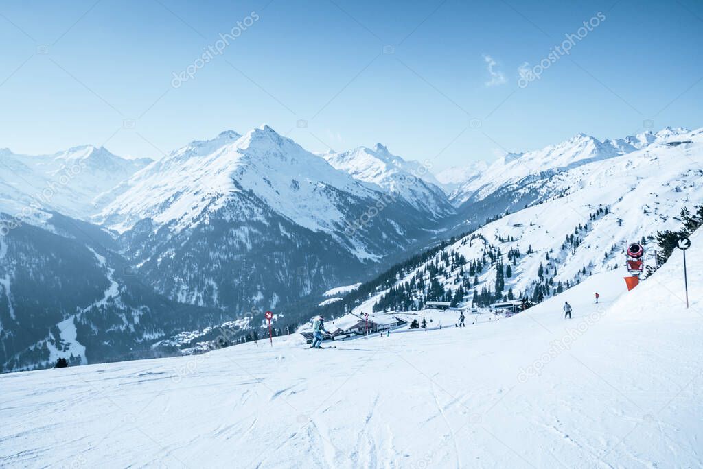 Skiers skiing on snow covered landscape. Beautiful white mountain range against sky. People enjoying winter sport in alps.