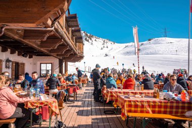 Aziz Anton am Arlberg. 10 Mart 2022. Kayak tatili sırasında kayak merkezindeki masaların yanındaki açık kafede oturan insanlar güneşli bir günde dağ kafesinde oturan turistler.