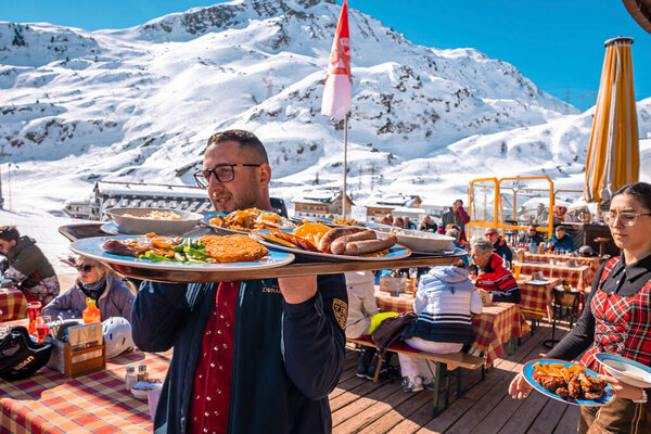 St. Anton am Arlberg. March 10, 2022. Waiters carries tray with fresh food while walking beside tables at outdoor cafe, Waiters carrying tray of dishes at mountain cafe on sunny day