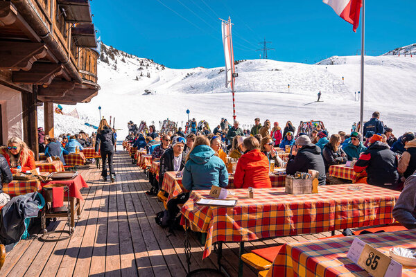 St. Anton am Arlberg. March 10, 2022. People sitting at outdoor cafe beside tables at ski resort chalet during skiing holiday, Tourists sitting at mountain cafe on sunny day
