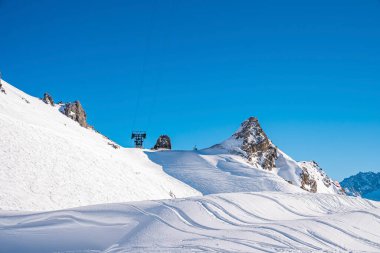 Cennet gibi beyaz bir arazide kayak izleri. Açık mavi gökyüzüne karşı dağları kaplayan manzaralı kar. Kışın güneşli bir günde Alpler.