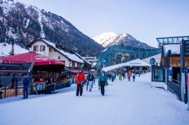 Aziz Anton am Arlberg. 10 Mart 2022. Kayak merkezindeki kayak salonlarında kayak yapan insanlar, karlı dağlara karşı kayak merkezinin yanında yürüyen kayakçılar.