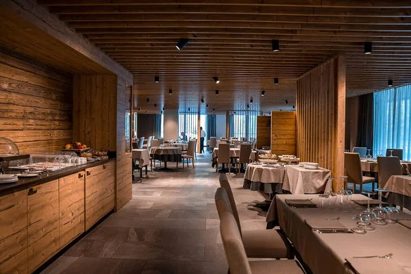 Geniş bir restoranda sıralanmış masa ve sandalyeler. Lüks kayak merkezinde kırsal tarzda yemek yenilen bir yer. Oteldeki yemek salonunun içi.