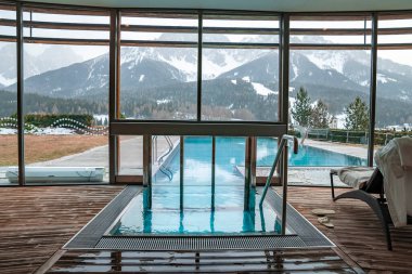 Tatil köyündeki yüzme havuzuna doğru. Camdan görünen karlı dağlar. Kış boyunca arka plandaki Alplerin manzarası.