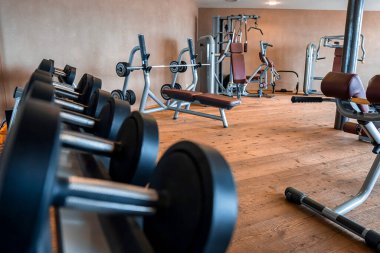 Modern spor salonunda çeşitli ekipmanlar var. Tatil evindeki ahşap zeminde düzenlenmiş makineler. Lüks oteldeki fitness merkezinin içinde..