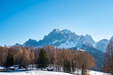 Dağlara karşı ağaçlarla kaplı karlı bir ev manzarası. Kışın açık mavi gökyüzüne karşı güzel bir manzara. Cennet alp bölgesinin görünümü.