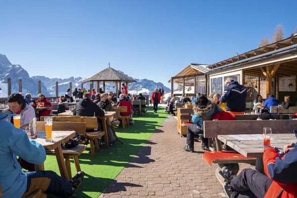 San Candido, İtalya. 18 Mart 2022. Kayak tatili sırasında kayak merkezindeki masaların yanındaki açık kafede oturan insanlar güneşli bir günde dağ kafesinde oturan turistler.