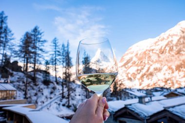 Madde boynuzu dağına karşı şarap kadehi tutan kadın. Kar kasabayı ve gökyüzünü kapladı. Turist kış tatilinde içki içiyor..