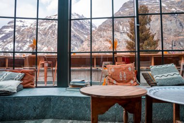 Pencere kenarındaki renkli yastıklar. Kış boyunca camdan görkemli dağ manzarası. Lüks kayak merkezinde şık bir oturma yeri..