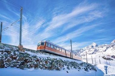 Kırmızı tren Gornergrat İstasyonu 'na doğru ilerliyor. Mavi gökyüzünün karla kaplı manzarası. Alplerde kış boyunca güzel manzara.