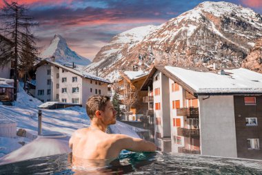 Gün batımında havuzda yüzen turistleri düşünüyorum. Güzel madde boynuzu dağları ve gökyüzüne karşı evler. İnsanın kışın jakuzide dinlendiği arka plan görüntüsü.