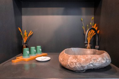 Benzersiz taş şekilli lavabo. Ahşap yüzeyde tek kullanımlık bardaklar. Lüks kayak merkezinin gri köşesinde lavabonun düzenlediği kurumuş çiçek vazoları.