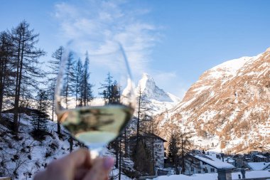 Güzel manzaraya karşı şarap kadehini tutan kadının bulanık görüntüsü. Güzel madde boynuzu dağı ve odağında karla kaplı kasaba manzarası. Kış boyunca Alp bölgesindeki Idyllic manzarası