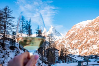 Kar kaplı madde boynuzu dağının manzarası ve gökyüzüne karşı kasaba manzarası. Şarap kadehi manzaralı bulanık bir kadın görüntüsü. Kış boyunca Alp bölgesinin güzel manzarası