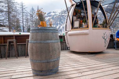 CERVO Oteli, Zermatt, İsviçre. 15 Mart 2022. Fıçının üzerinde vazoyla süslenmiş kurumuş çiçekler. Oteldeki oval şekilli tezgahta çalışan bir işçi. Lüks otellerden görünen dağların manzarası.