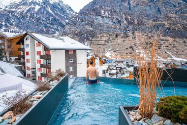 CERVO Oteli, Zermatt, İsviçre. 15 Mart 2022. Dağlara ve evlere bakarken havuzda yüzen bir turist. Jakuzide rahatlayan bir adamın arka görüntüsü. Kış boyunca Alpler 'in manzarası.