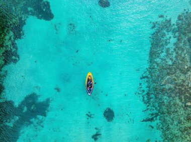 Aerial view of yellow kayak in blue lagoon at summer. Man on a floating canoe in clear azure water, rocks, stones. Mallorca, Spain. Tropical landscape. Sup board. Active travel. Top view