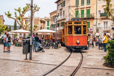 Mallorca, İspanya. 27 Nisan 2022. Tren raylarında hareket eden ünlü tramvaya bakan turistler. Erkekler ve kadınlar şehri geziyor. Geleneksel tarihi tren eski kasabadaki binalara çarpıyor..