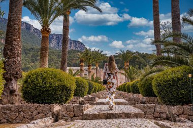 Çiçeklerin arasında yürüyen kadın turistler. Günlük giyinmiş bir kadın tarihi parkı keşfediyor. Yaz tatilini adada geçiriyor..