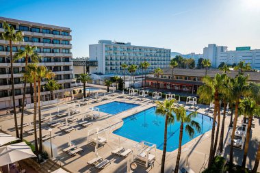 Yüksek açılı yüzme havuzlu tatil köyü manzarası. Berrak gökyüzüne karşı şezlongları olan modern lüks oteller. Yaz tatili kavramı.