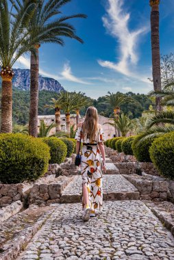 Çiçeklerin arasında yürüyen kadın turistler. Günlük elbiseli bir kadın tarihi parkı keşfediyor. Yaz tatilini adada geçiriyor..