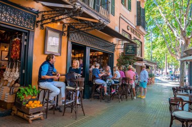 Mallorca, İspanya. 27 Nisan 2022. Erkek ve bayan turistler açık hava restoranında dinleniyorlar. İnsanlar boş zamanlarını tarihi şehirde geçiriyorlar. Yaz tatilinin tadını çıkarıyorlar..