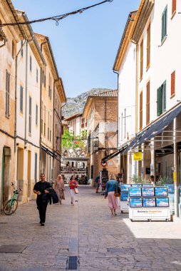 Mallorca, İspanya. 27 Nisan 2022. Turistler ara sokakta binaların arasında yürüyorlar. Açık mavi gökyüzüne karşı yerleşim bölgesindeki sokağa düşen gölge. Yaz tatilinde turizm.