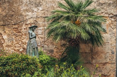 Bitkilerin arasındaki palmiye ağacının yanındaki kadın heykeli. Duvara karşı heykel. Doğanın ortasındaki yaratıcılık.